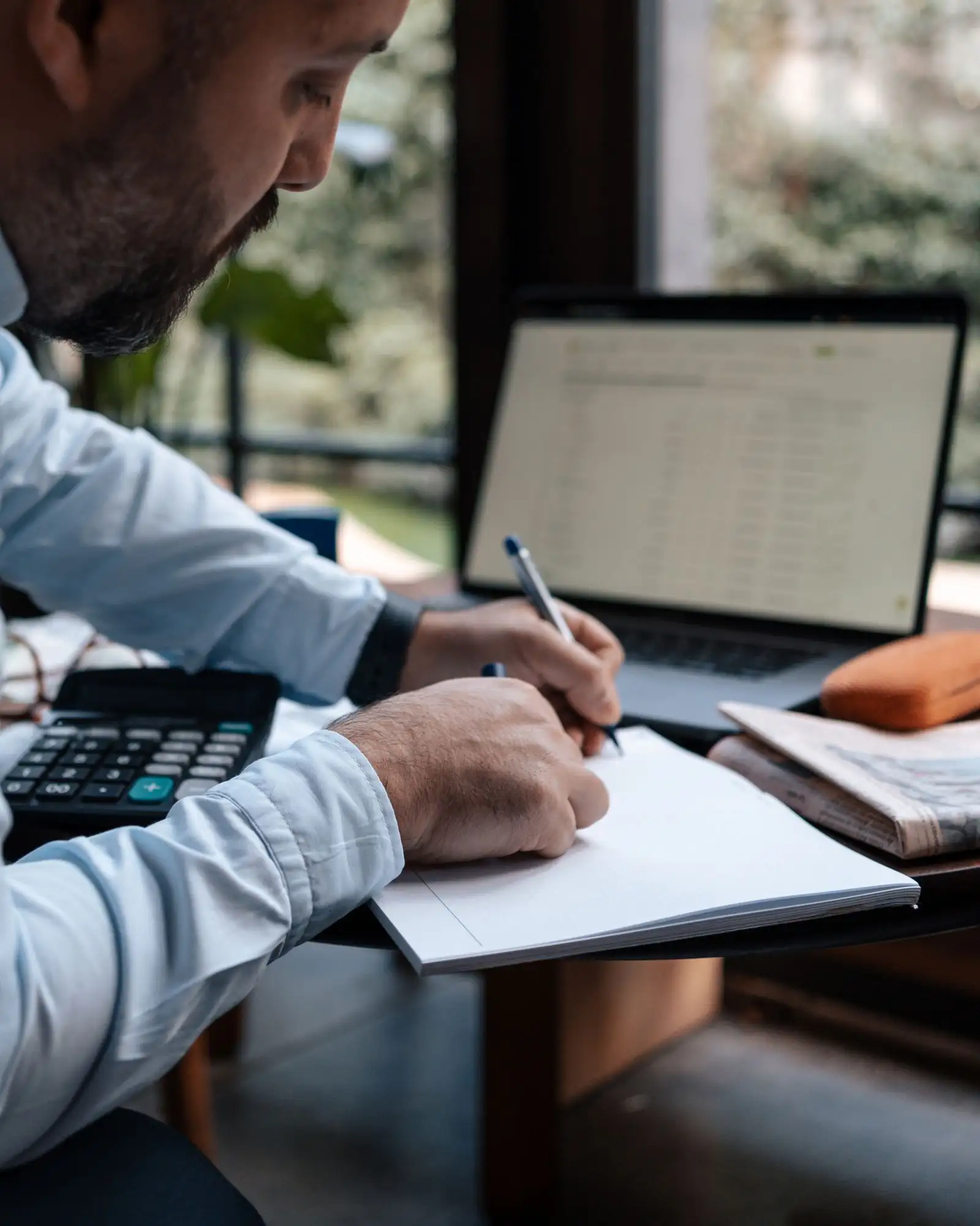 Manos con calculadora, laptop y libreta preparando una cotización