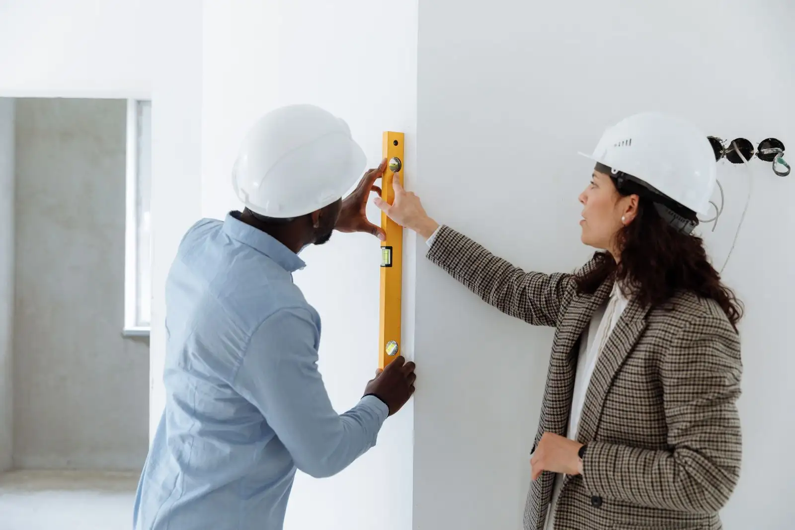 Un técnico mide una pared con un nivel mientras la clienta le señala